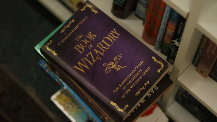 A fantasy novel resting on a stack of books, representing the newly revealed covers for ACOTAR 6 and 7